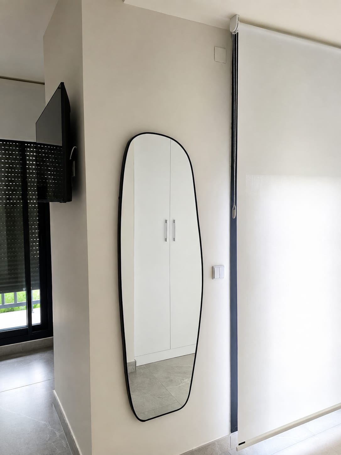 Espejo, estor y televisión colgados en una pared de pladur de un salón